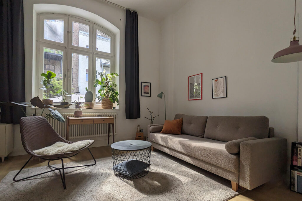 Altbauzimmer mit Sessel, Tisch und Sofa vor einem großen alten Bogenfenster