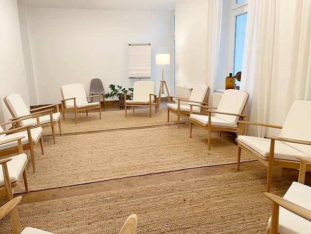 Altbauzimmer mit Sessel, Tisch und Sofa vor einem großen alten Bogenfenster
